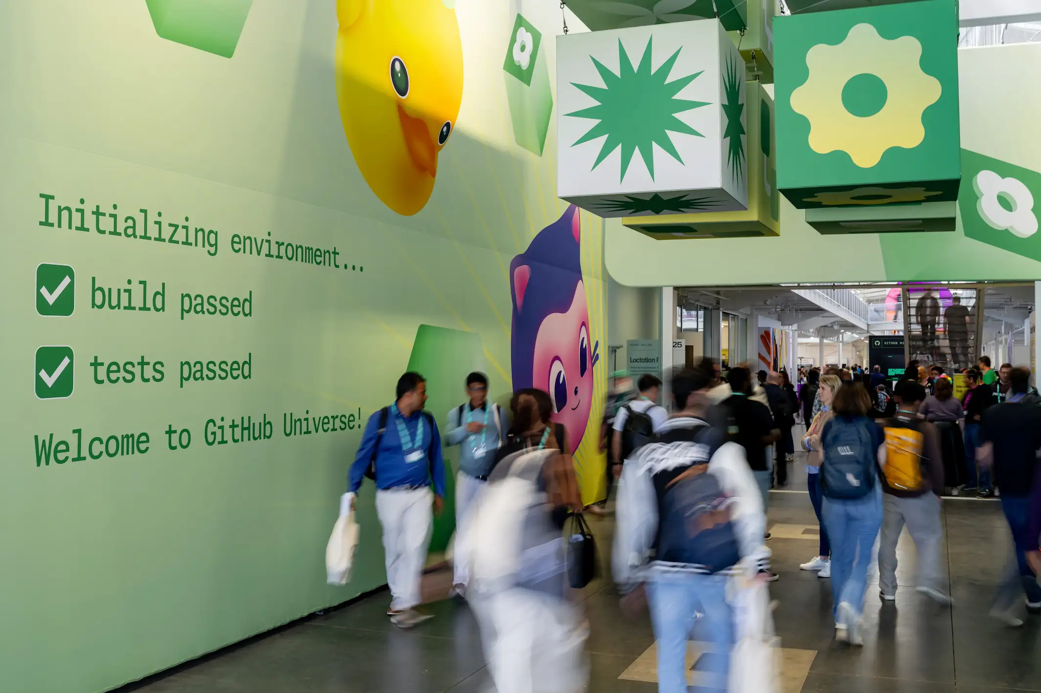 Attendees walk through a busy GitHub Universe hallway with colorful graphics and welcome signage on the walls.